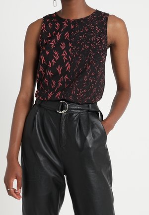 Top negro sin mangas con estampado de hojas rosas metido en pantalones de cuero negros de cintura alta con cinturón y hebilla de doble anilla.