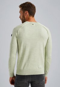 Hellgrüner Pullover mit strukturiertem Finish, langen Ärmeln und Rundhalsausschnitt. Besitzt einen dekorativen Knopf auf der Rückseite und gerippte Bündchen.
