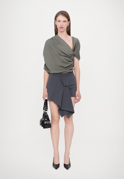 Olivengrøn draperet top med korte ærmer, parret med en grå asymmetrisk ribbet miniskirt, og sorte høje hæle. Sort håndtaske inkluderet.