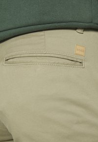 Beiga byxor i ett texturerat tyg, med slim fit och en bakficka. Logotypen är präglad på en rektangulär läderlapp.