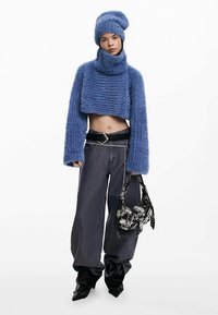 Blå, dunet cropped sweater og matchende beanie, kombineret med vide mørke jeans og en sort mønstret håndtaske. Glat tekstur, oversized pasform.