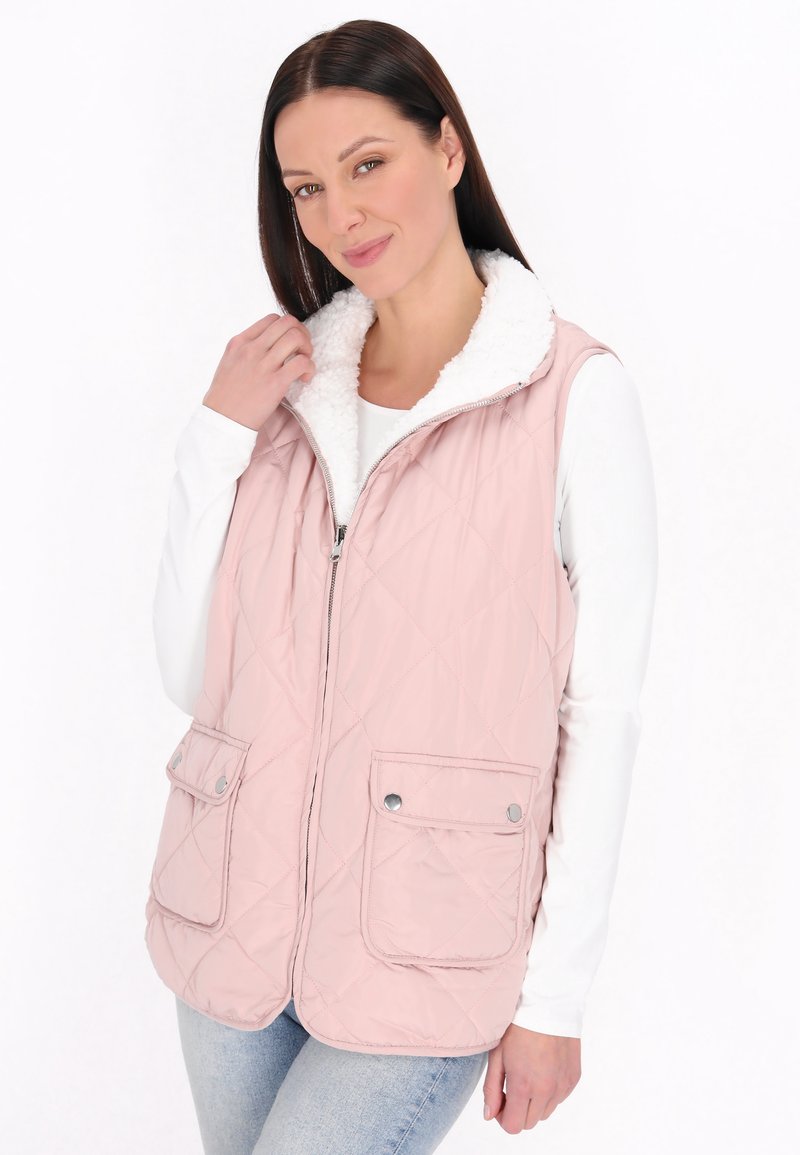 Gestepptes pinkes Westchen mit einem weißen Fleece-Kragen, zwei Fronttaschen und Reißverschluss, getragen über einem weißen Langarmshirt.
