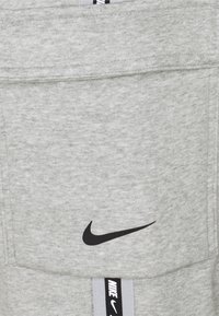 Šedá mikina vyrobená z jemné tkaniny. Obsahuje černé logo Nike a kontrastní šedý pruh s textem "NIKE". Jednoduchý design s kapsami.
