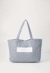Stripete stoff totebag i marineblått og hvitt, med flat topp, to håndtak og en hvit lapp med preget tekst. Lett og romslig.