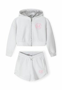 Hoodie bianca in cotone con zip, design corto e logo circolare rosa; pantaloni corti bianchi abbinati con vita elastica e dettaglio del logo.