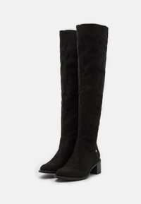 Black over-the-knee boots made of soft suede. Features a block heel, rounded toe, and minimalistic design with a small logo accent.