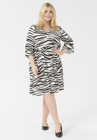 Zebradesign-Kleid in Schwarz und Weiß, lockerer Schnitt, knielang, mit Kragen und drei Viertelärmeln. Glatter Stoff.