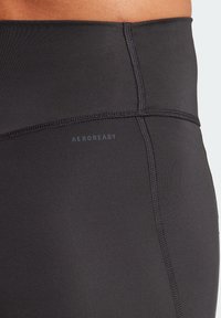 Close-up van zwarte sportleggings met zichtbare stiksels en het "AEROREADY" logo aan de zijkant nabij de taille.