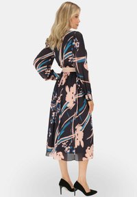 Sukienka w kwiaty z długimi rękawami, wciągnięta w talii i o zwiewnym kroju. Charakteryzuje się ciemnym tłem z jasnoróżowymi i niebieskimi akcentami. Czarne szpilki.