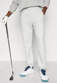 Γκρι φούτερ παντελόνι με ελαστική μέση και πλευρικές τσέπες, συνδυασμένα με λευκά αθλητικά παπούτσια με ναυτικές λεπτομέρειες και μια γκολφ.