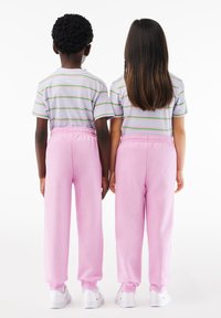 Deux enfants portant des t-shirts rayés gris avec des rayures roses et vertes, associés à des pantalons de survêtement roses et des baskets blanches, vus de dos.