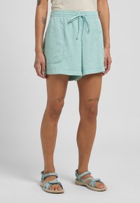 Hellblaue Shorts mit einem elastischen Bund und Kordelzug. Sie verfügen über seitliche Taschen und einen lockeren Schnitt, kombiniert mit türkisfarbenen Sandalen.