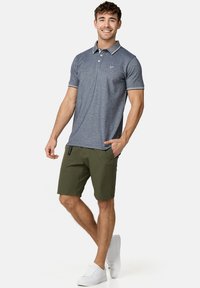Marineblauwe polo met een contrasterende kraag, gecombineerd met olijfgroene shorts. De outfit heeft witte accenten en casual witte sneakers.