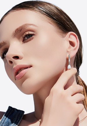 Zilveren hangers met een heldere druppelsteen, met een gedraaide ringontwerp. Close-up van een model dat de sieraden toont.