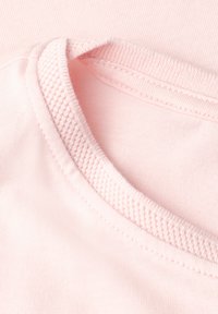 Gros plan d'un tissu rose montrant l'encolure texturée et les détails de couture d'un vêtement en coton doux.