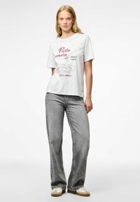 Camiseta blanca con un diseño gráfico de pasta y texto en burdeos y negro, combinada con jeans de pierna ancha grises y zapatillas.