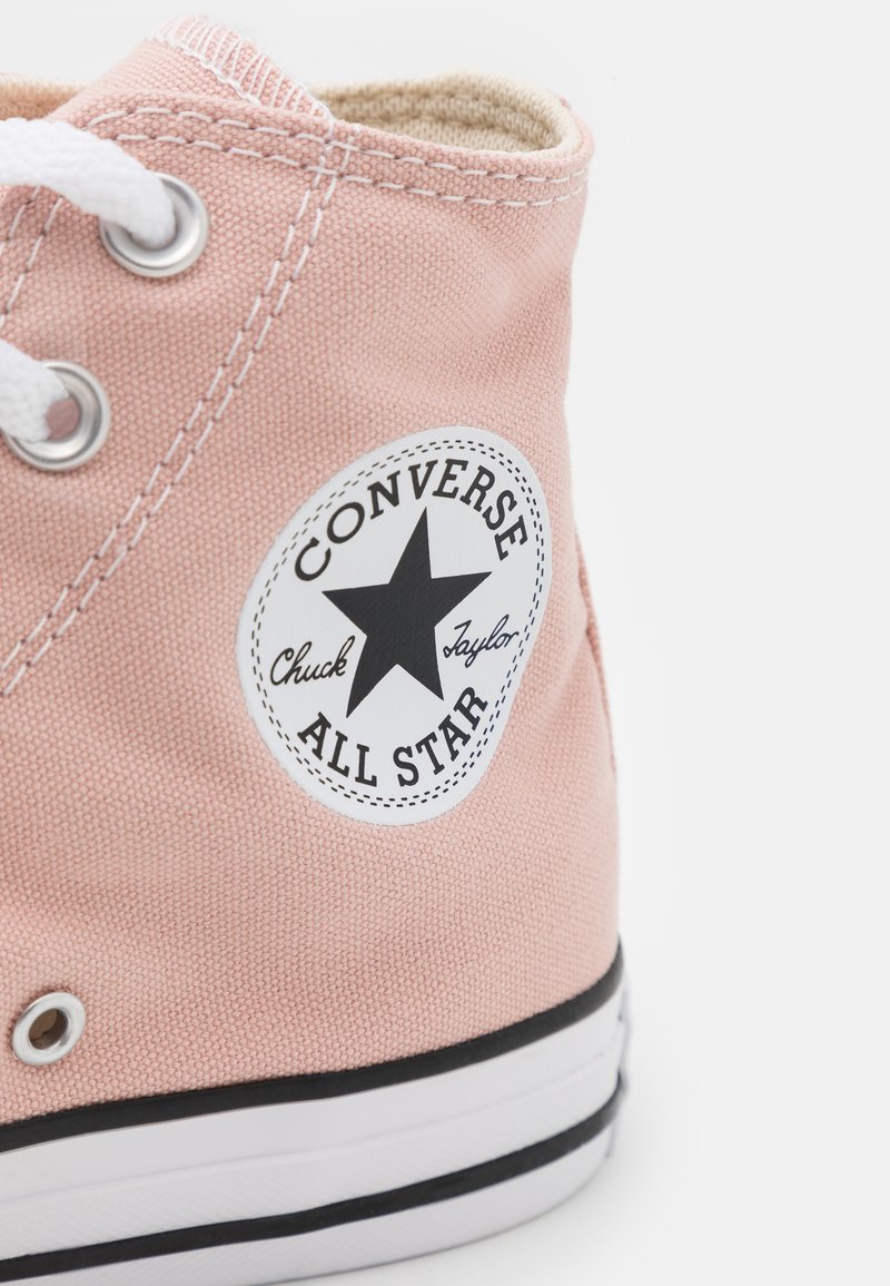 Zapatilla alta de lona rosa con cordones blancos, parche de logo en blanco y negro, y suela de goma negra con una franja blanca.
