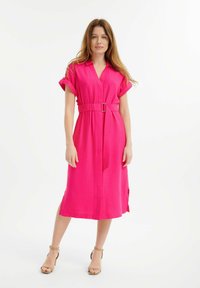 Abito rosa, fino al ginocchio, con maniche corte, scollatura a V e vita con cintura. Tessuto morbido, motivo discreto e spacchi laterali per il movimento.