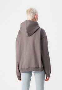 Overdimensjonert grå hettegenser med stor hette, ribbestrikkede mansjetter og kant, laget av mykt stoff, sammen med lys blå tettsittende jeans.