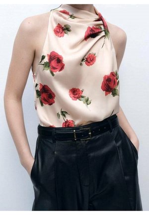 Satynowy top w kremowym kolorze z czerwonymi różami, z dekoltem wzdłuż szyi, noszony z wysokim stanem czarnych skórzanych spodni i czarnym paskiem.