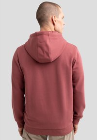 Bordeauxfarbener Hoodie aus weichem Stoff, mit einer verstellbaren Kapuze und gerippten Bündchen. Die Rückansicht zeigt eine glatte Textur mit minimalen Designdetails.