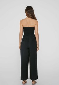 Mono negro con un cuerpo sin mangas fruncido, pantalones de pierna ancha y una tela ligera. La vista trasera muestra una textura suave y un ajuste relajado.