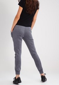 Šedé joggingové kalhoty s tapered nohavicemi, elastickými manžetami a bočními kapsami, spárované s černým tričkem s krátkým rukávem a černými teniskami.