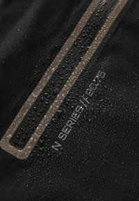 Kapi vode na crnoj tkanini s reflektirajućim uskim okomitom trakom i tekstom "N SERIES 178" utisnutim blizu trake.