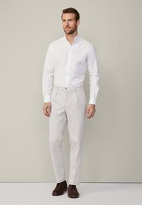 Witte overhemden met knopen, lichtgrijze broek, bruine suède schoenen. Rechte snit, gladde textuur en minimale ontwerpelementen door het hele kledingstuk.