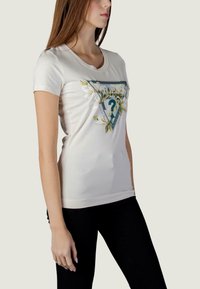 T-shirt blanc en coton à manches courtes, avec un imprimé graphique triangulaire vert et floral. Coupe droite avec un col rond.