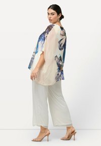 Lichte, semi-doorzichtige blouse in crème met blauwe bloempatronen, gecombineerd met losse, witte palazzo-broeken en blote hakken in nude.