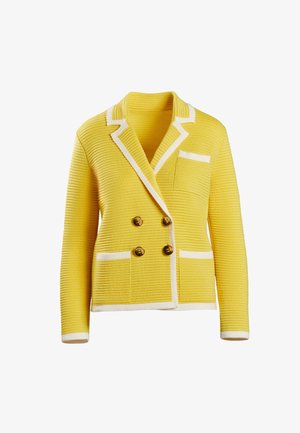 Geel dubbelgebreid jasje met ribbelstructuur, witte accenten, gouden knopen en een borstzak. Lange mouwen met witte manchetten.