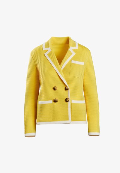 Sárga, dupla mellényes kabát bordázott textúrával, fehér kiegészítőkkel, arany gombokkal és egy mellzsebből. Hosszú ujjakkal, fehér mandzsettával végződik.