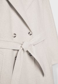 Manteau en laine beige clair à double boutonnage avec de gros boutons et une ceinture en tissu assorti, nouée à la taille.
