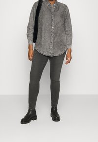 Grå denimskjorta med långa ärmar och knappar, i kombination med mörkgrå tajta jeans och svarta ankstövlar med kraftiga sulor.