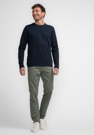Navyblauwe long-sleeve shirt gecombineerd met lichtolijfgroene broek en witte sneakers. Het shirt heeft een ronde halslijn en een aansluitende pasvorm.