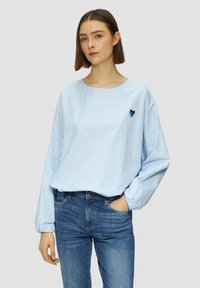 Camicia a maniche lunghe a righe blu e bianche con scollatura rotonda e dettaglio ricamato a forma di cuore. Abbinata a jeans di denim blu.