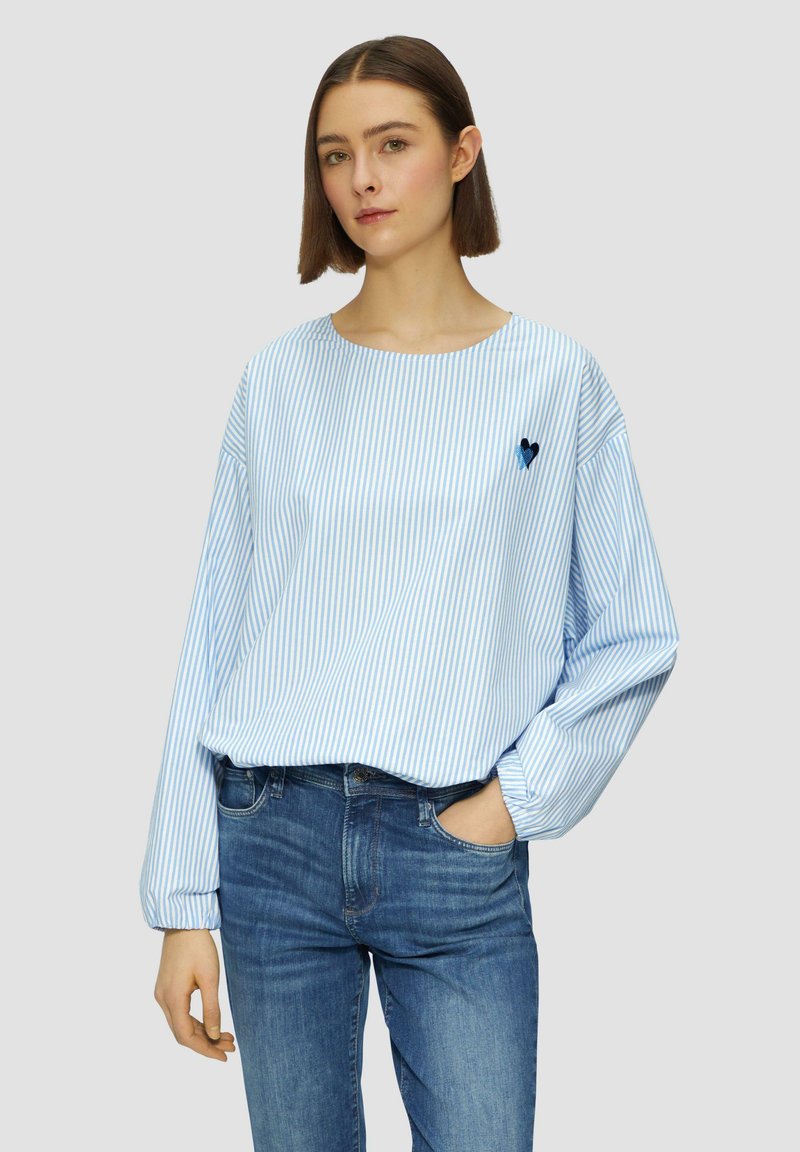 Camicia a maniche lunghe a righe blu e bianche con scollatura rotonda e dettaglio ricamato a forma di cuore. Abbinata a jeans di denim blu.