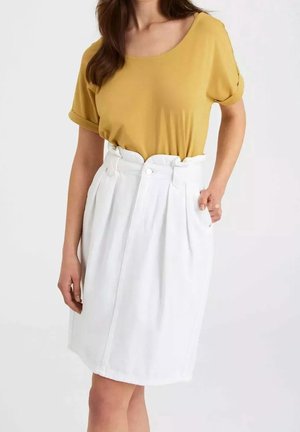 Mujer con un top de manga corta color mostaza metido dentro de una falda blanca de cintura alta, de longitud hasta la rodilla, con pliegues y detalle de botón.