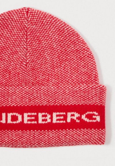 Gorro de punto rojo con un patrón de hilos rojos y blancos alternos. Presenta una banda de letras en bloque blanca cerca de la base.