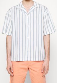 Chemise à manches courtes avec boutons, en tissu léger, présentant des rayures verticales bleues et blanches, un col campagnard et une coupe décontractée.