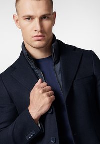 Granatowy płaszcz z wełny z domieszką z wykrojem w serek oraz zapinaną na zamek podszewką, z zapięciem na guziki i teksturowanym detalem materiału.