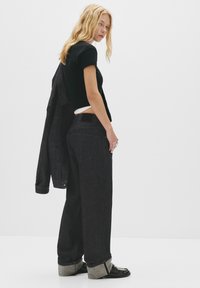 Zwarte denim jeans met een losse pasvorm, met opgerolde manchetten en achterzakken. Gecombineerd met een zwarte getailleerde t-shirt en een denim jack.