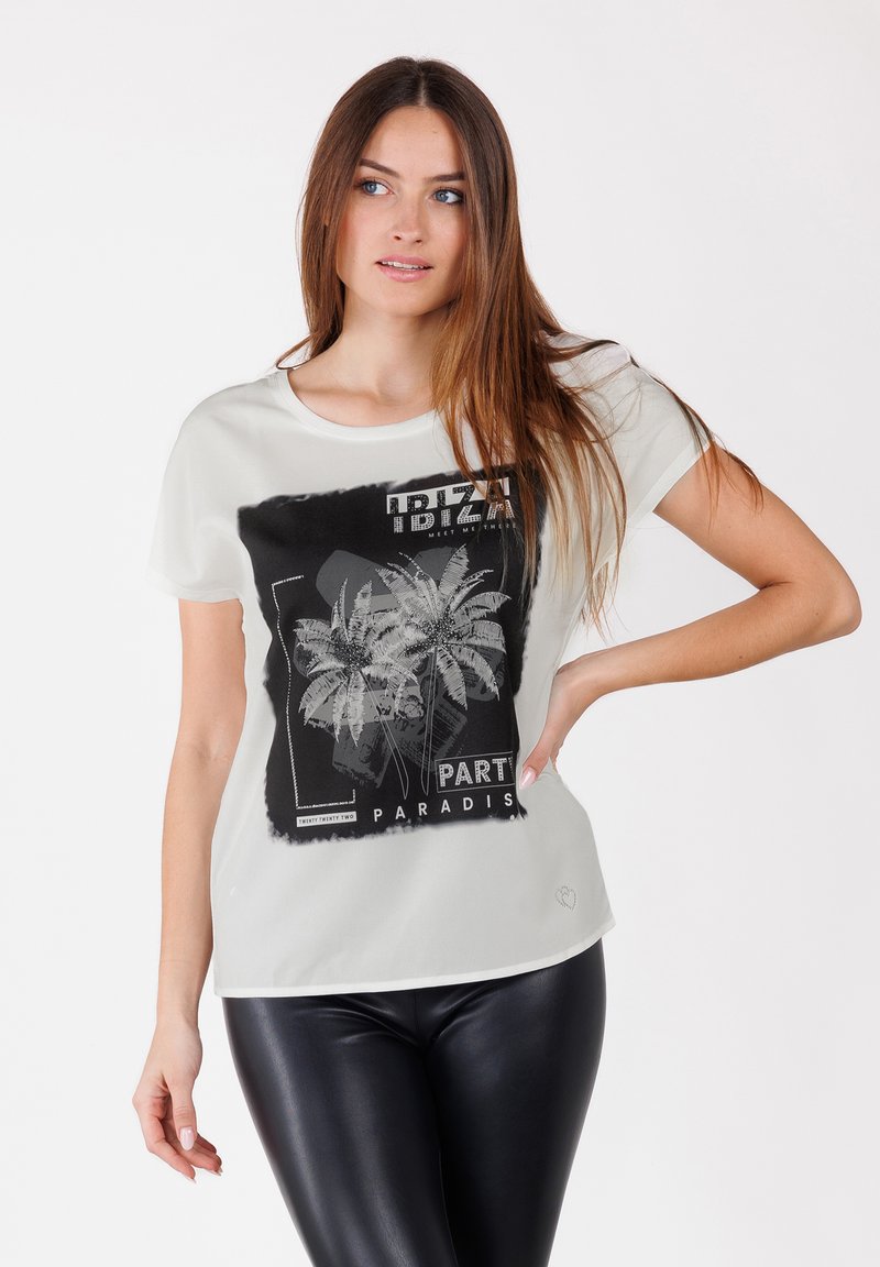 Camiseta blanca con un gráfico de palmera negra, que presenta el texto "IBIZA PART PARADIS" en negrita. Cuello redondo, mangas cortas, ajuste relajado.