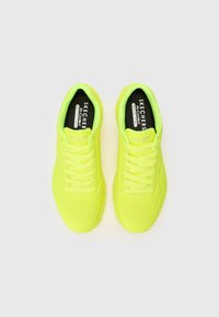 Baskets de sport jaune fluo avec tige en mesh, design perforé, languette rembourrée et lacets plats ; présente la marque "SKECHERS" sur la semelle intérieure.