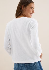T-shirt blanc à manches longues en tissu léger, avec un col rond et une coupe décontractée, associé à un short en denim bleu.