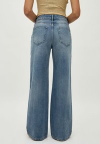 Wide-leg blue denim jeans feature a high waistband, two back pockets, and a raw hem, with a soft, textured finish.