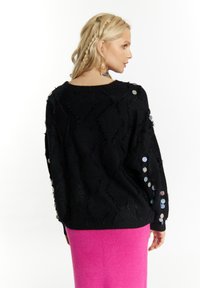 Pulover negru din tricot, cu un model texturat în zigzag și accente metalice dispersate pe mâneci, asortat cu o fustă roz aprins.