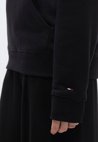 Μαύρο φούτερ με ριμπ μανσέτες και τελείωμα, με ένα μικρό κόκ κινο, λευκό και μπλε λογότυπο στο μανίκι. Ομαλή υφή.