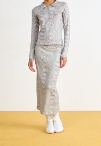 Grå, ribbad stickad koord-set som inkluderar en knapplångärmad topp och en matchande lång kjol, bärs med vita sneakers.